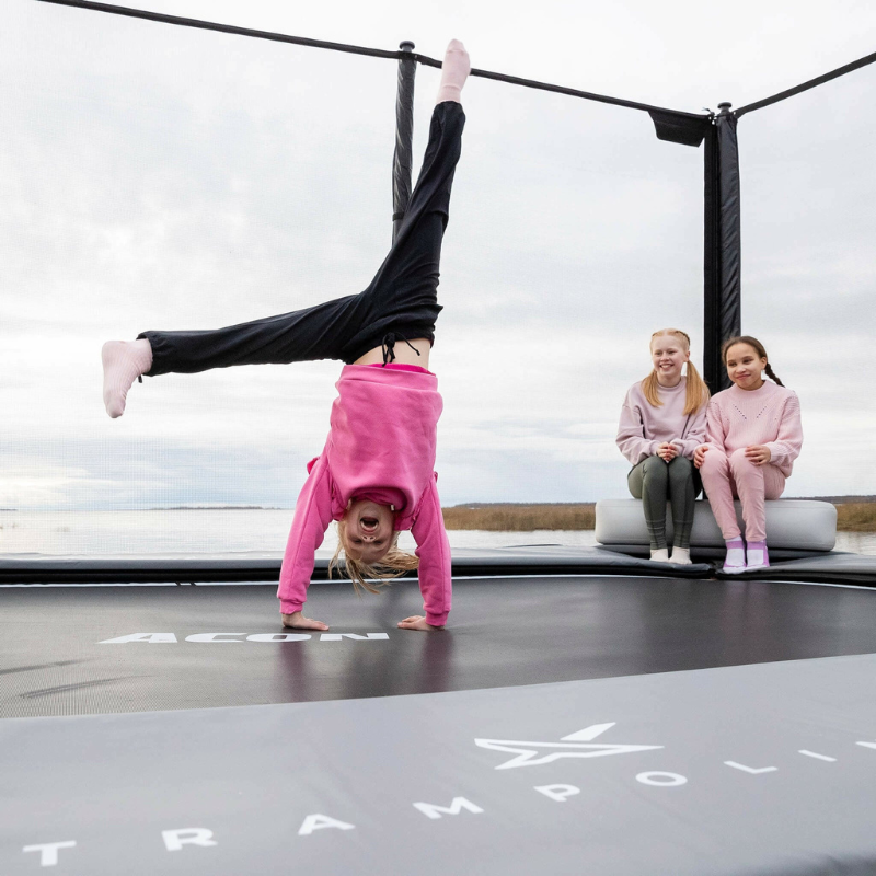 Child doing a handstand on a trampoline with two other children watching and sitting in ACON X Block.
