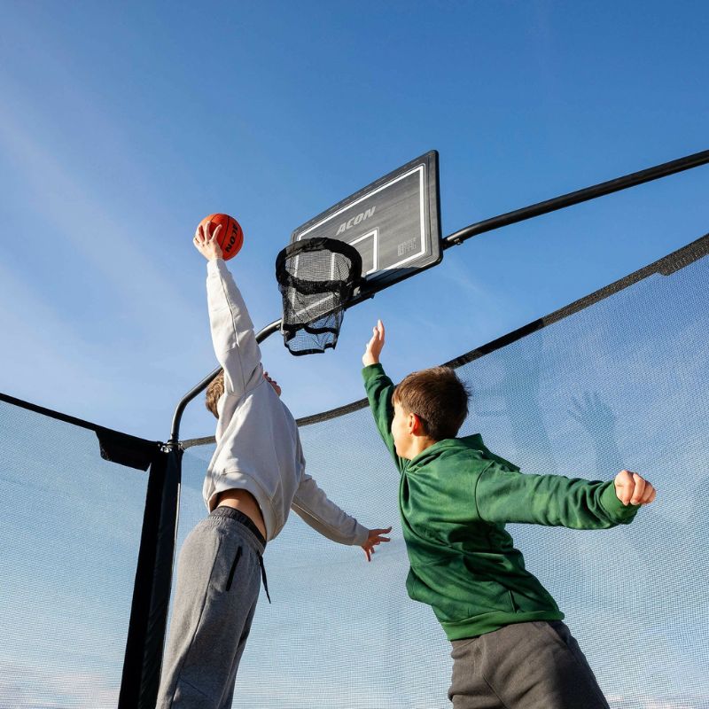 Two children playing basketball Hoop  set up in a trampoline clear blue sky.