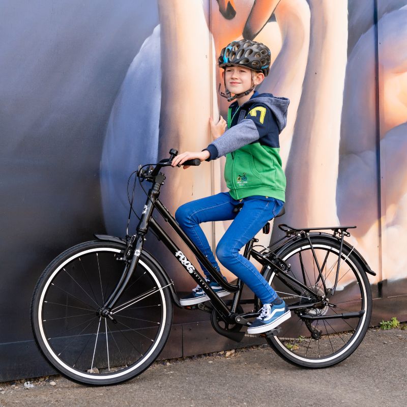 Child on a Frog City 61 bicycle wearing a helmet against a colorful wall.