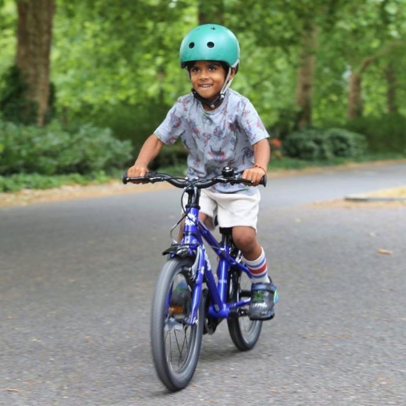 Child riding a Frog44 blue bicycle on a road with greenery in the background