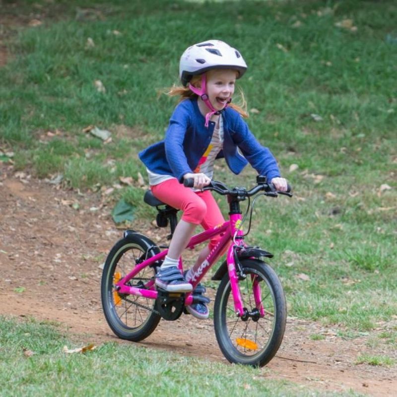 Child riding a Frog44 pink pedal bicycle on a grassy path