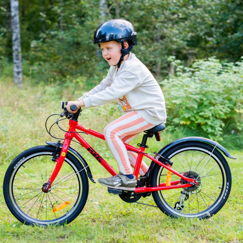 Child riding a red frog 53 bicycle in a grassy area with trees in the background