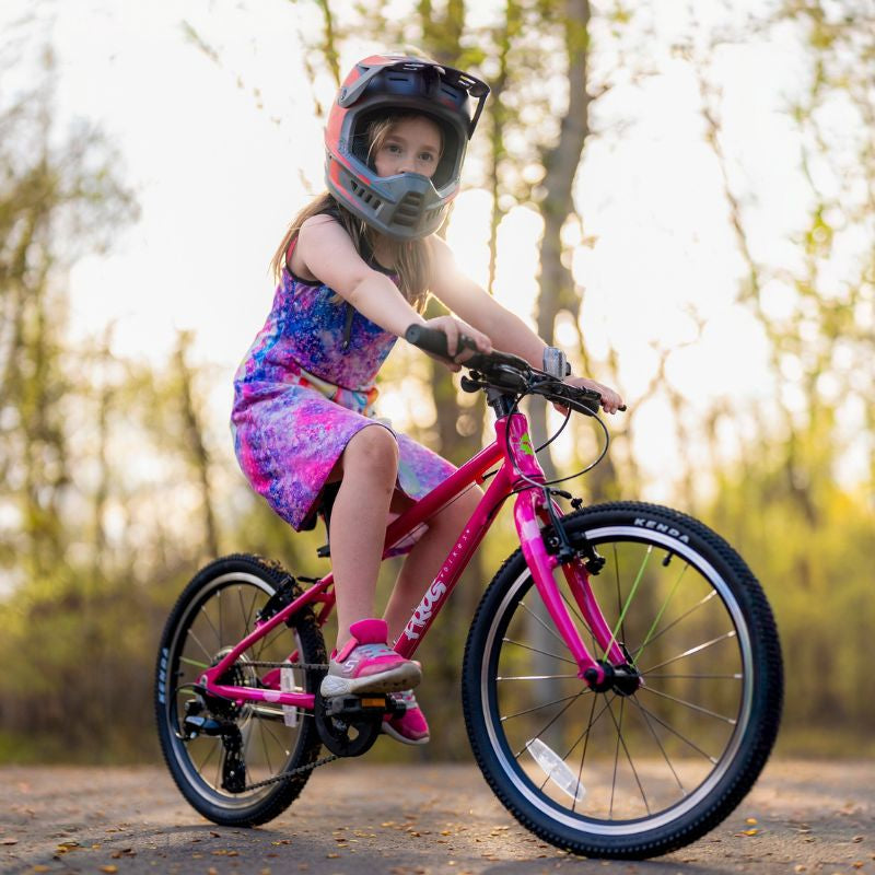 Child riding a pink frog 53 bicycle with a helmet in a forest setting