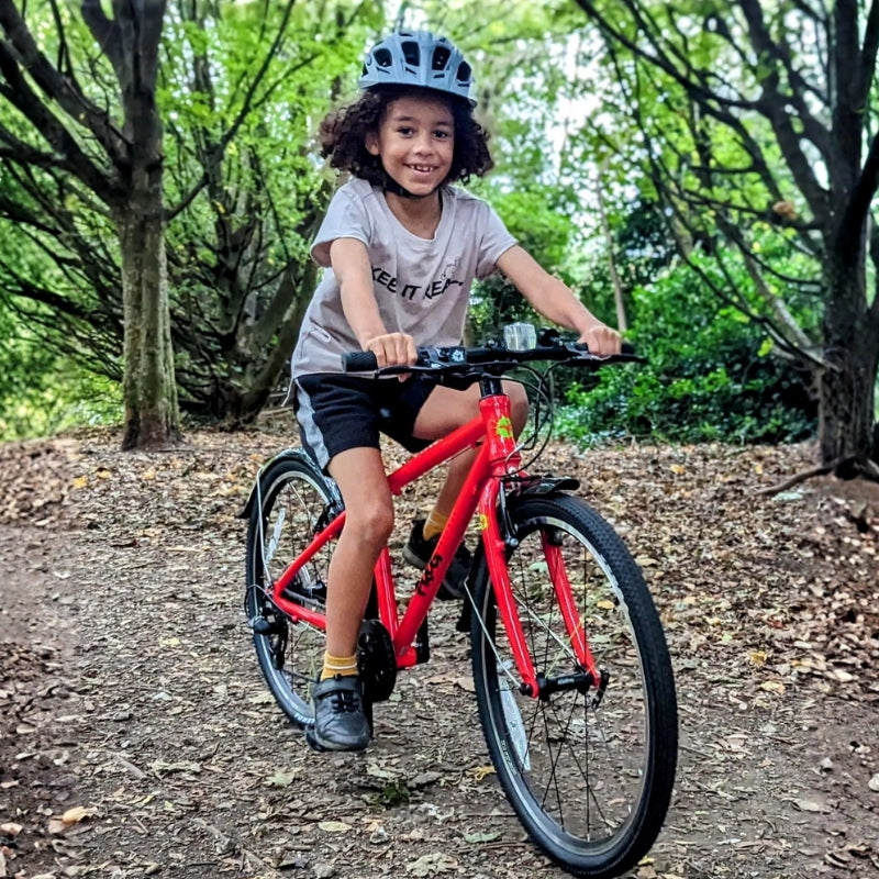 Child riding a red frog 61  bicycle on a trail with trees in the background