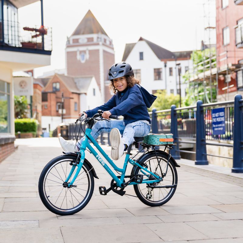 Child riding a blue city 53 bicycle with a helmet on a city street.