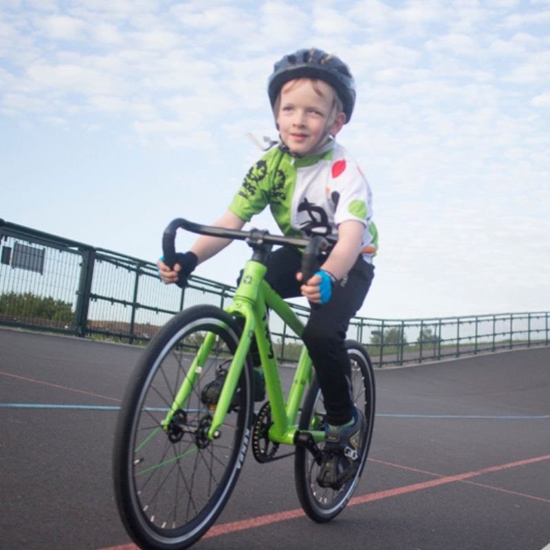 Child riding a Frog Track 58 green bicycle on a track with a blue sky background