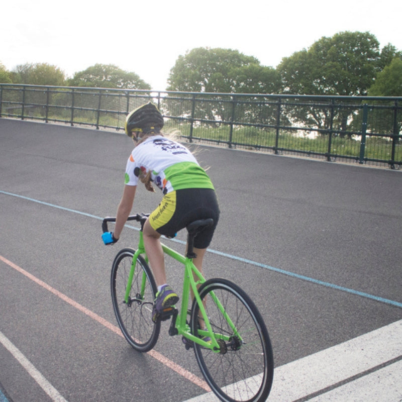 Young Girl riding a Frog Track 58 green bicycle on a paved road with trees in the background