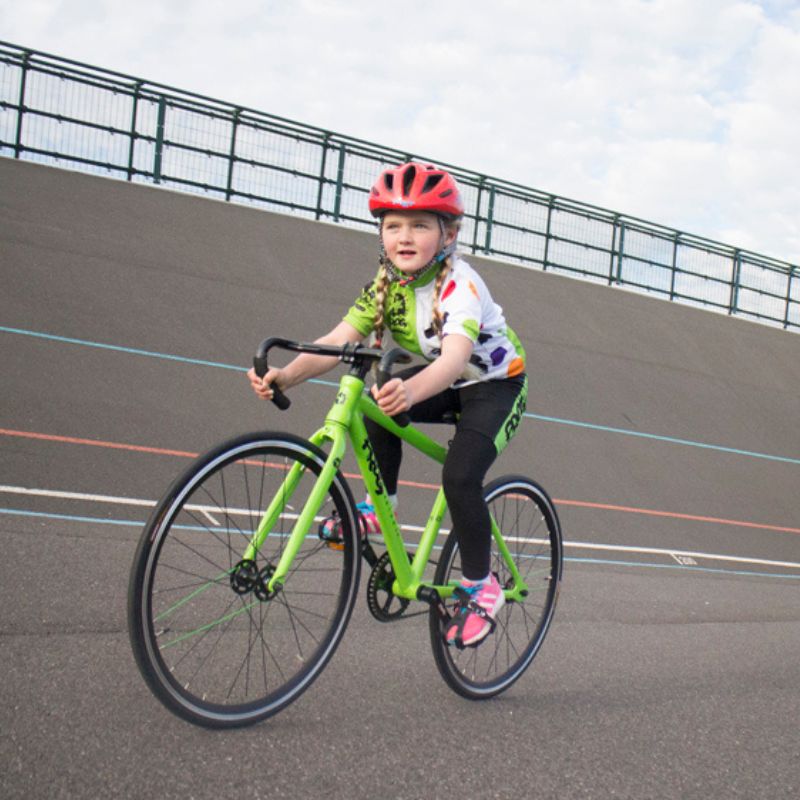 Child riding a  Frog Track 67 green bicycle on an outdoor track with a helmet on