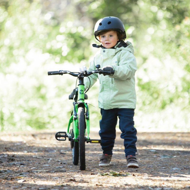 Child with a green bicycle wearing a helmet and light jacket outdoors.