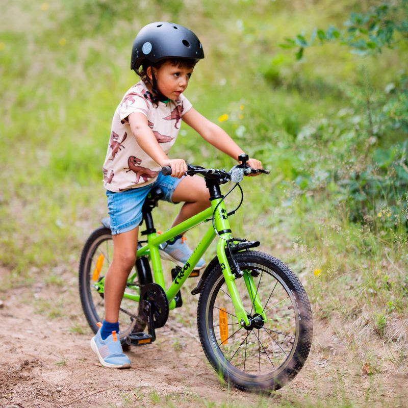 Child riding a green bicycle on a dirt path with grass and plants in the background
