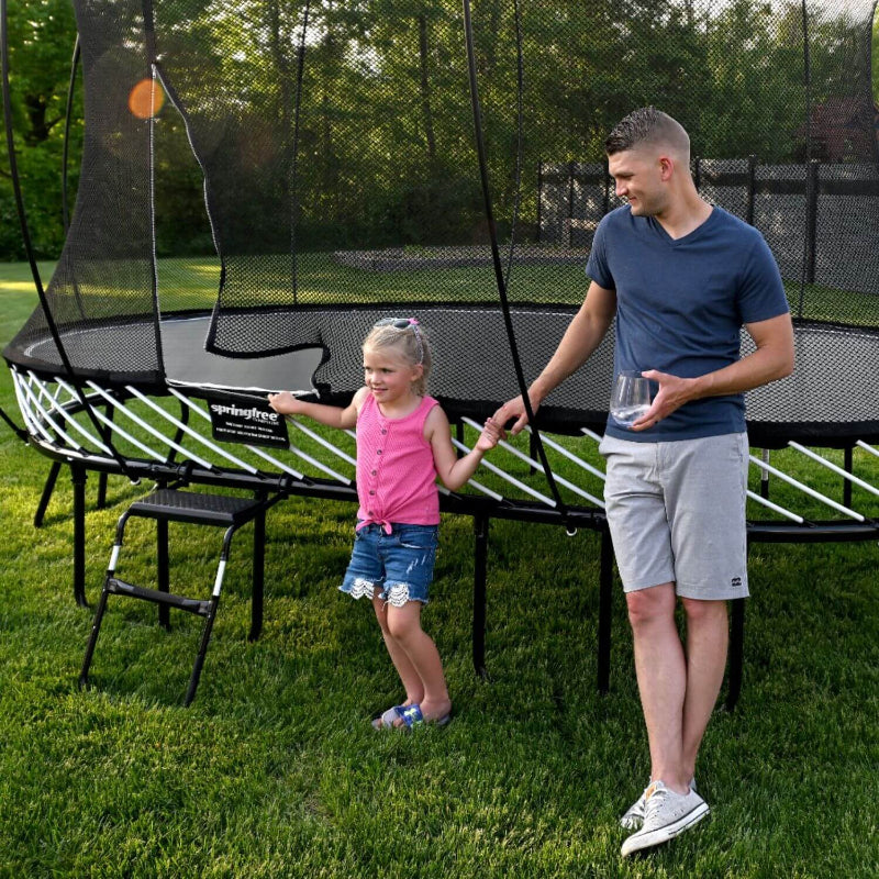 Father and Daughter standing besides Springfree® 8ft x 13ft Large Oval Trampoline 