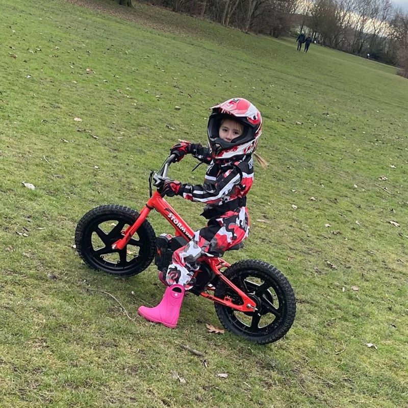 Child on a Red Storm Kids 170w Electric Balance Bike on a white background with a helmet and pink boots in a grassy field