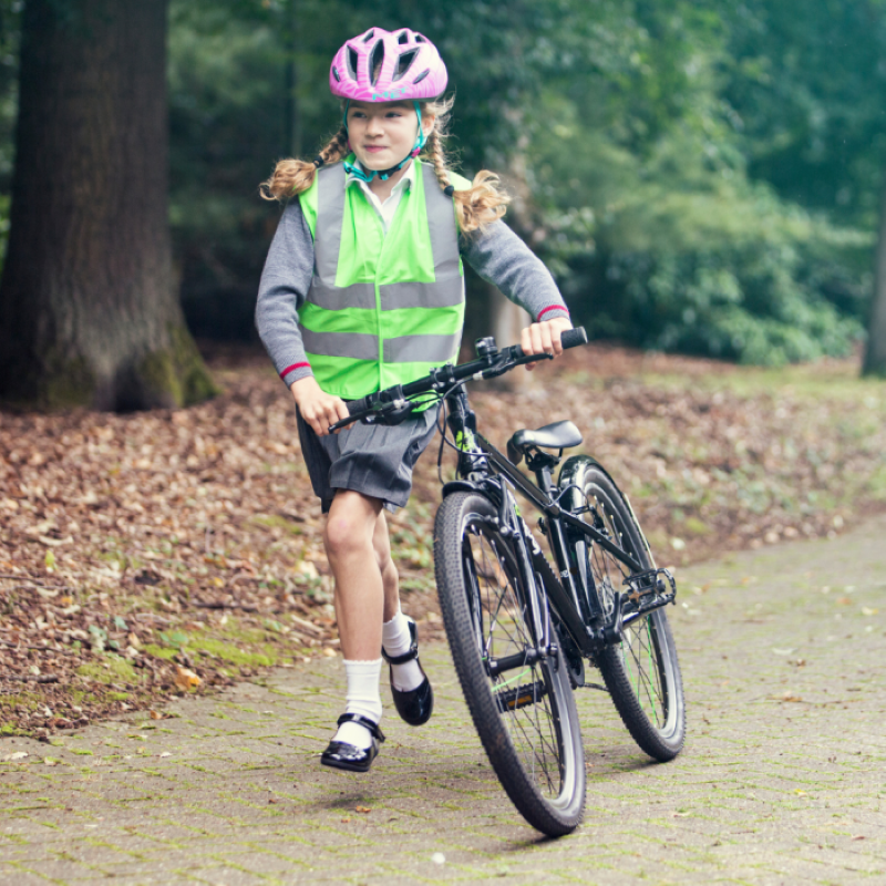 Child pushing her frog 67 bicycle on a path with trees in the background